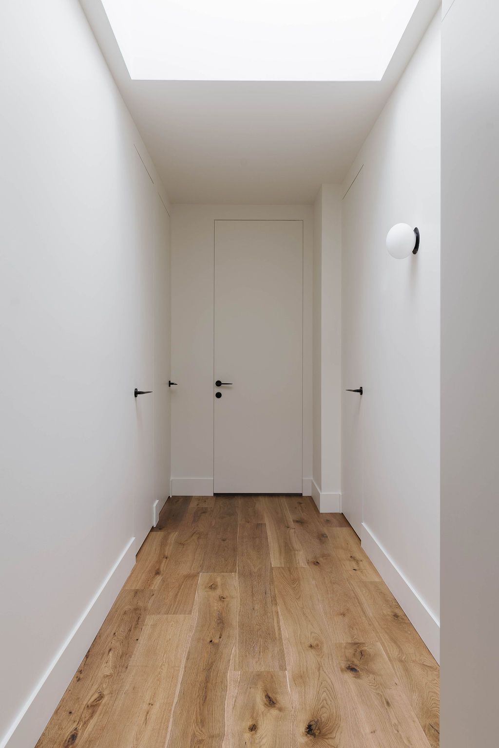 Un long couloir avec du parquet et des murs blancs.