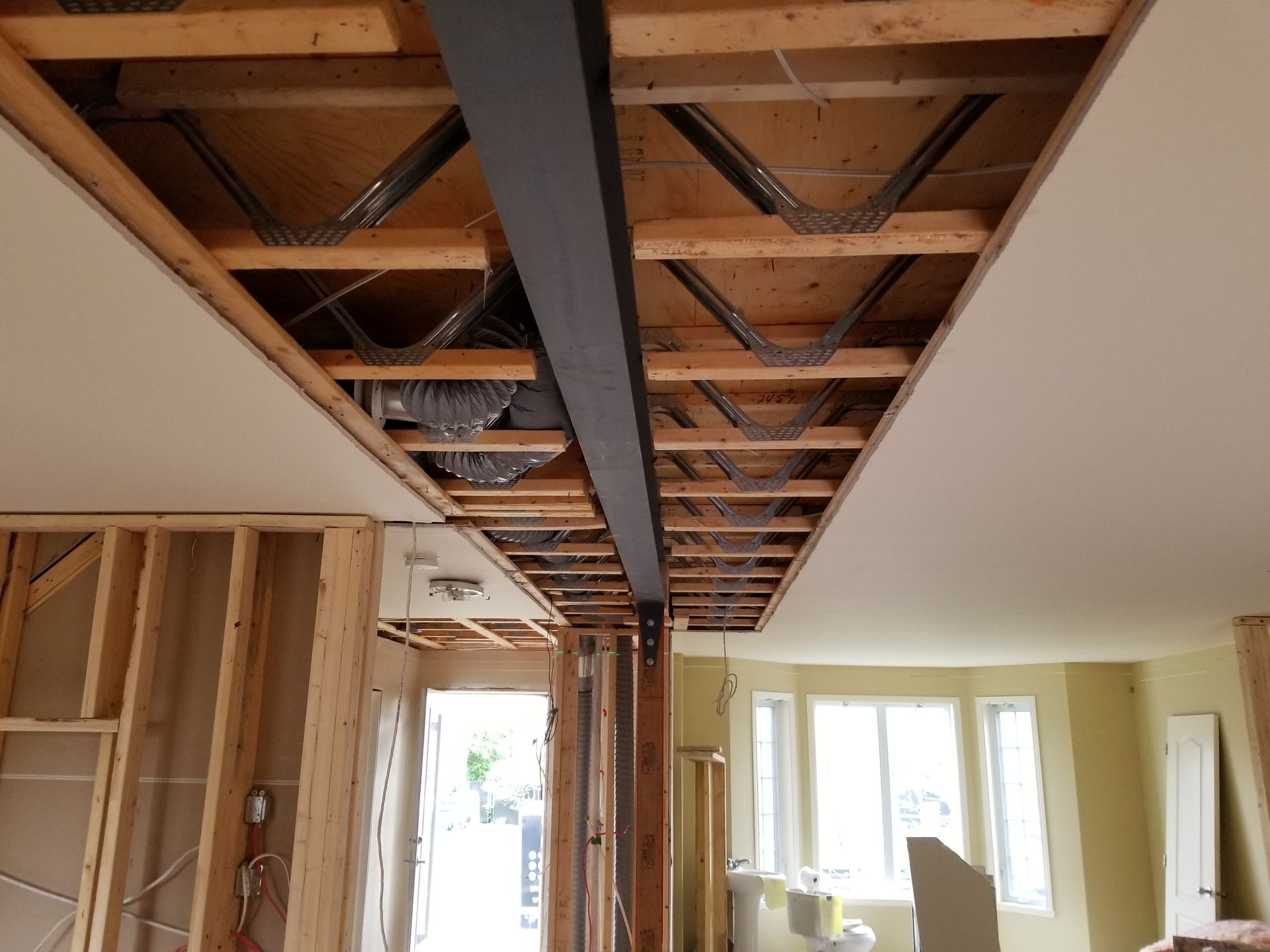 Intérieur d'une maison en rénovation montrant une poutre en acier noir soutenant la structure apparente du plafond.