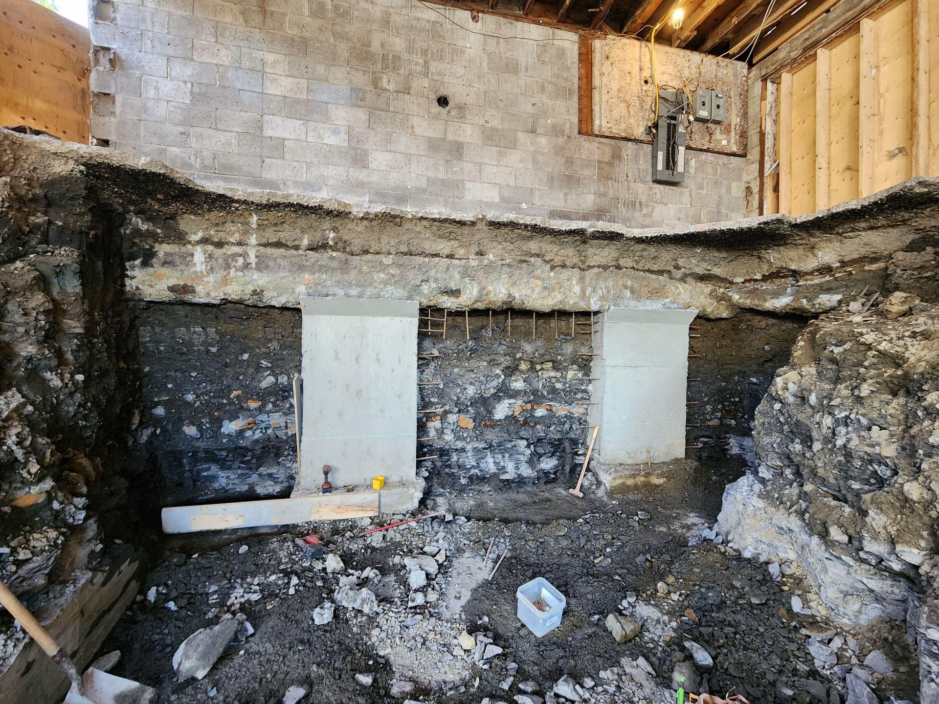 Excavation souterraine avec murs en pierre exposés et marquages orange sur fondations.