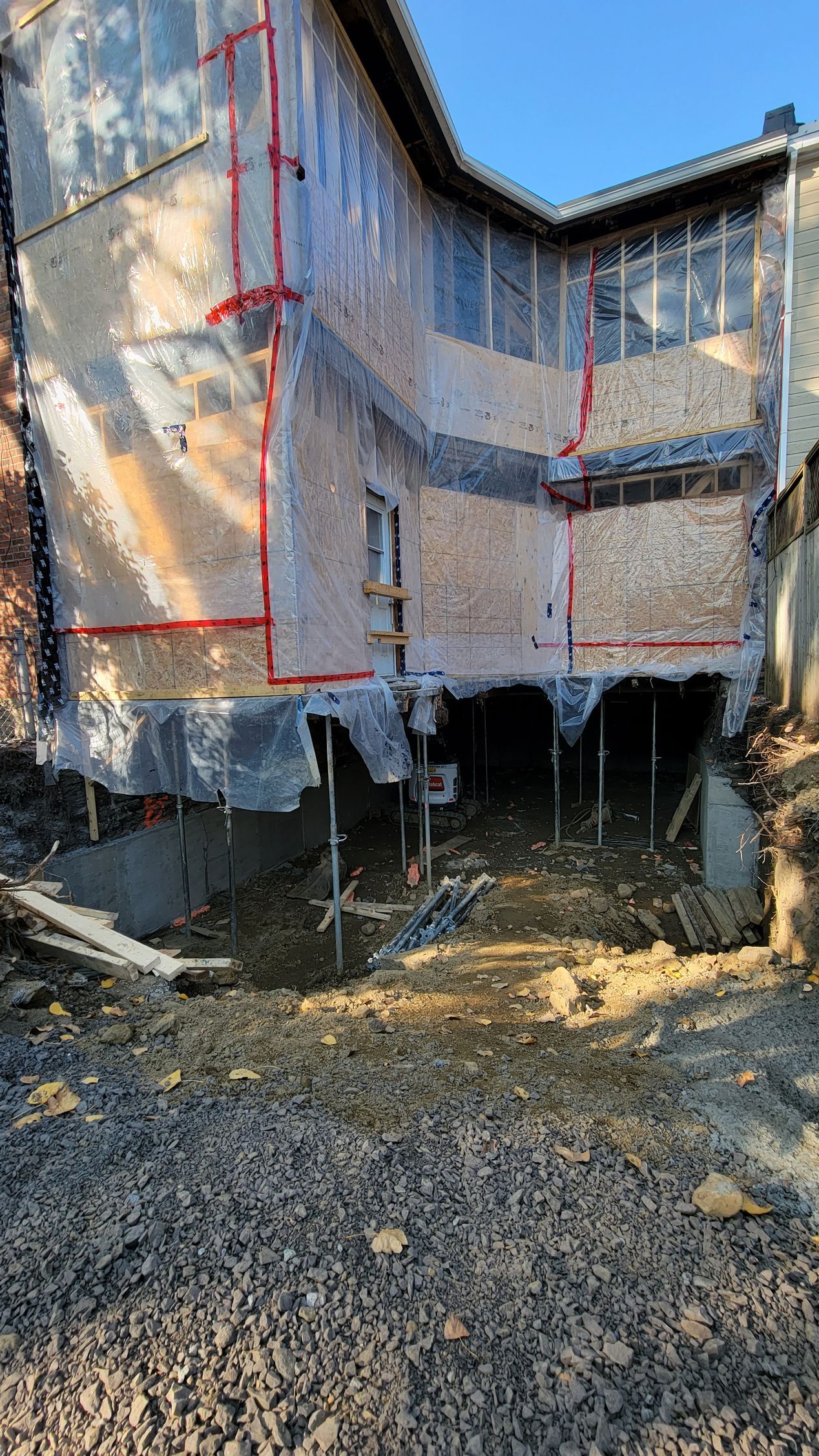 Maison en rénovation avec échafaudage, membrane de protection et marquages rouges aux murs.