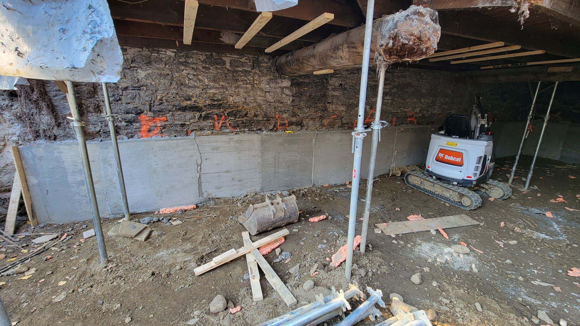 Intérieur d'un bâtiment en rénovation avec murs en pierre apparents, poutres en bois, équipement de construction et débris au