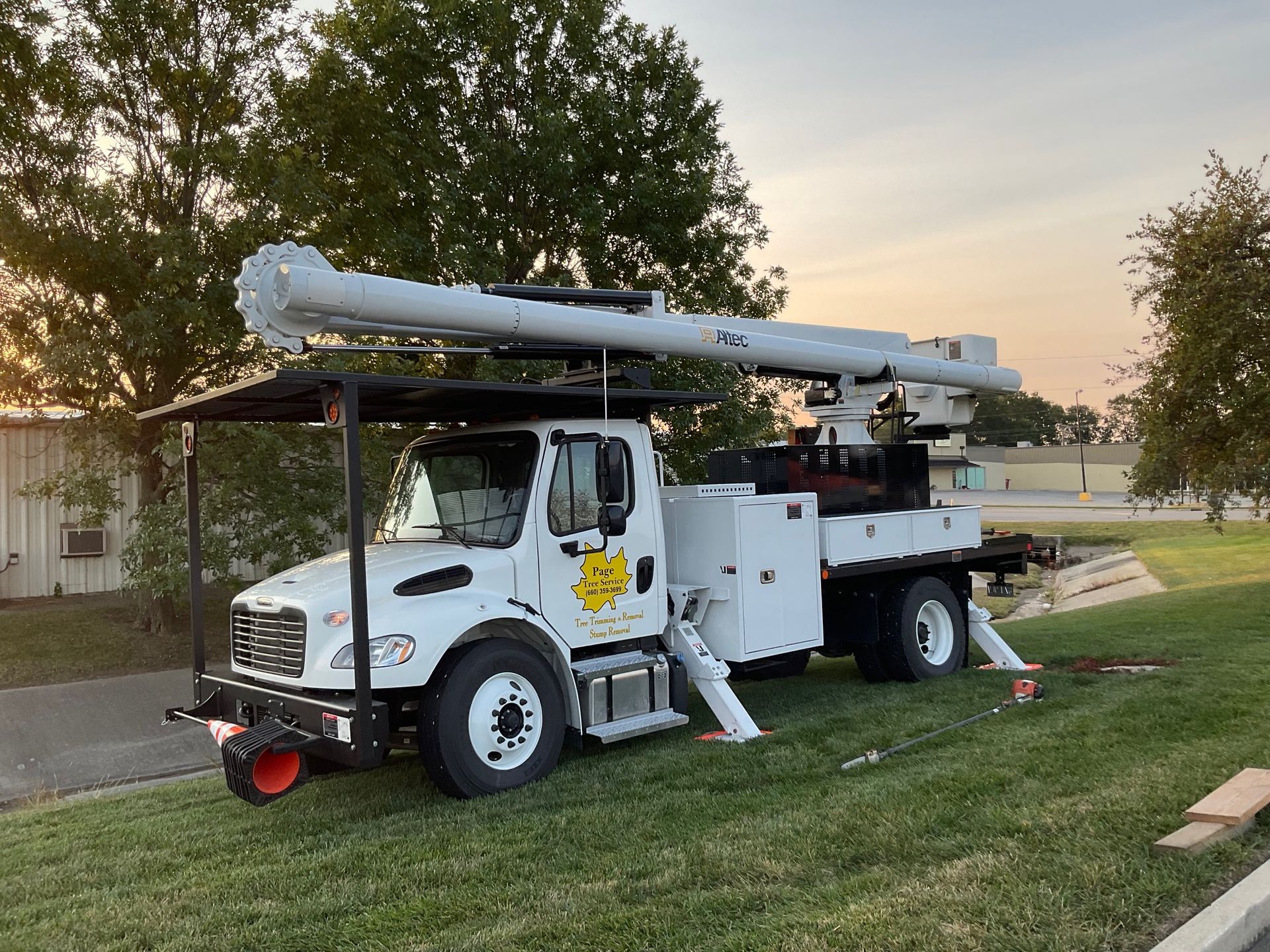 A white truck with a crane on top of it is parked in the grass.