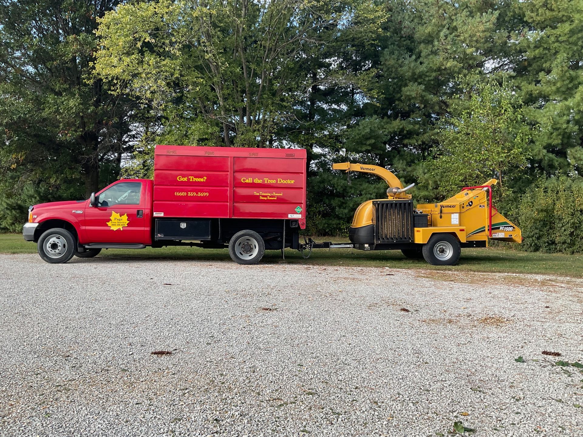 A red truck with a chipper attached to it is parked in a gravel lot.