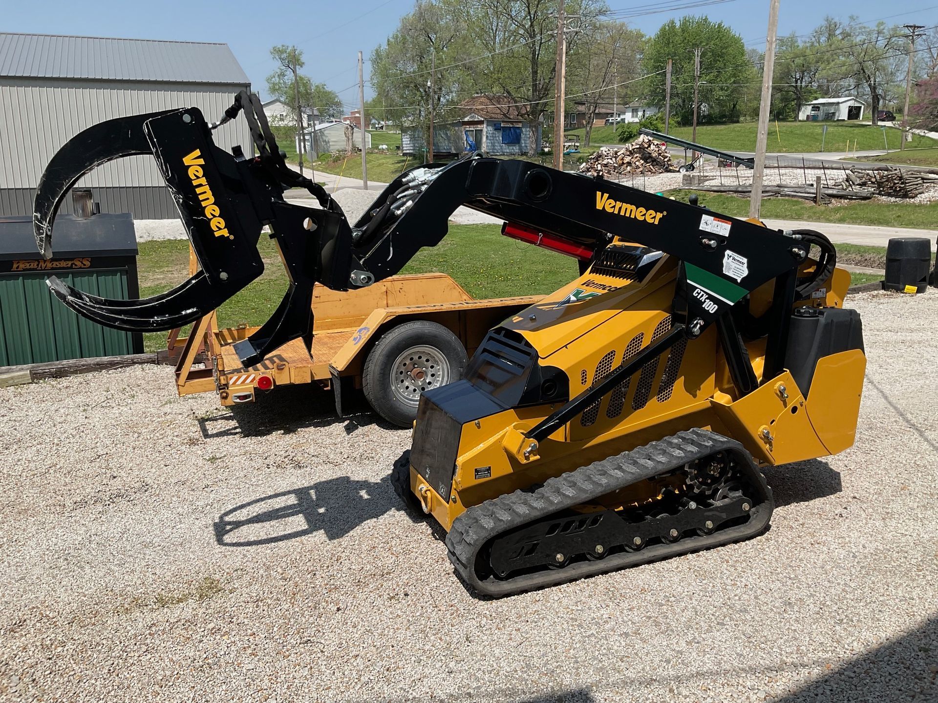 A yellow tractor with a black grapple attached to it is parked in a gravel lot.