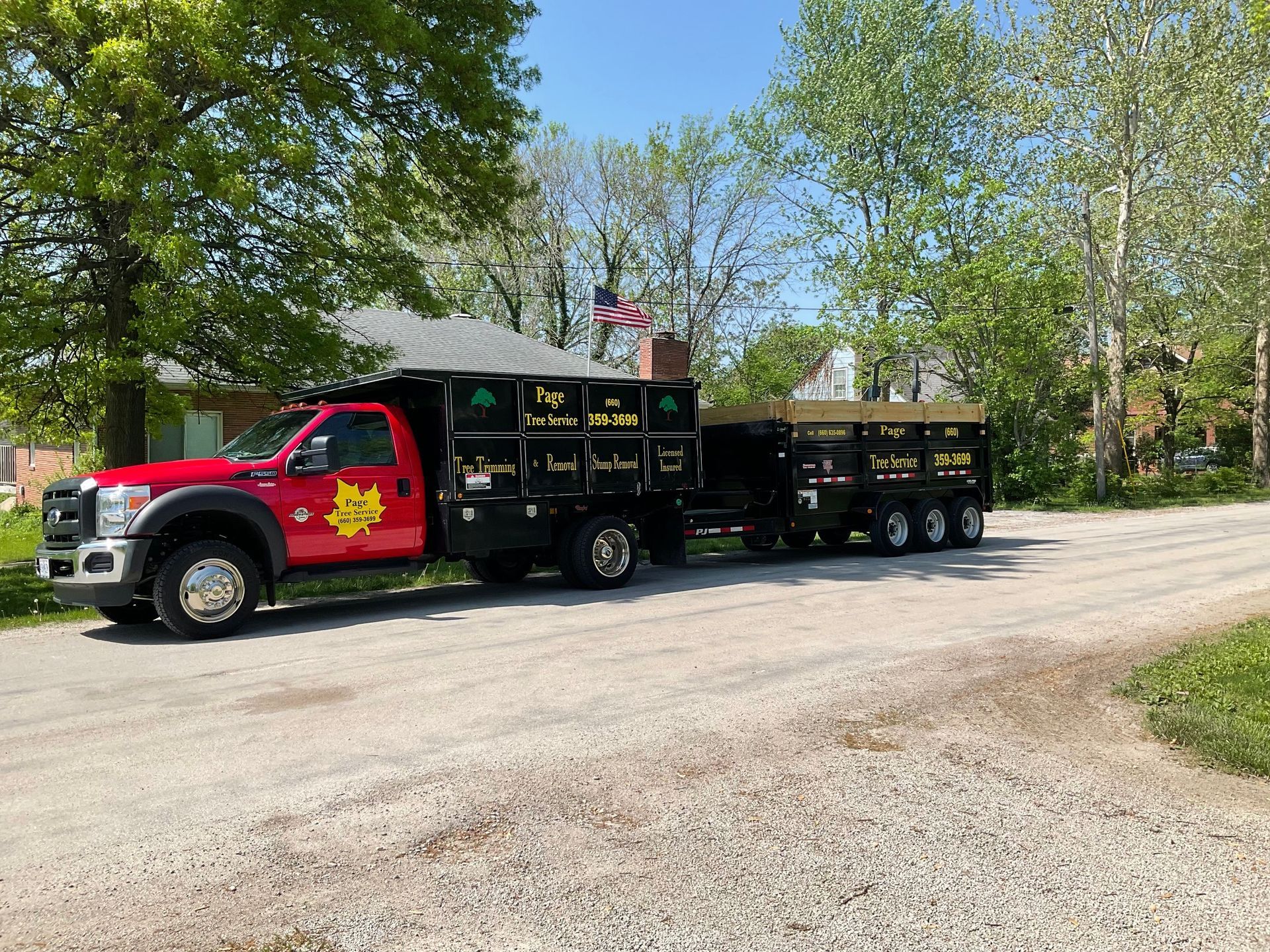 A red truck with a trailer attached to it is parked on the side of a gravel road.