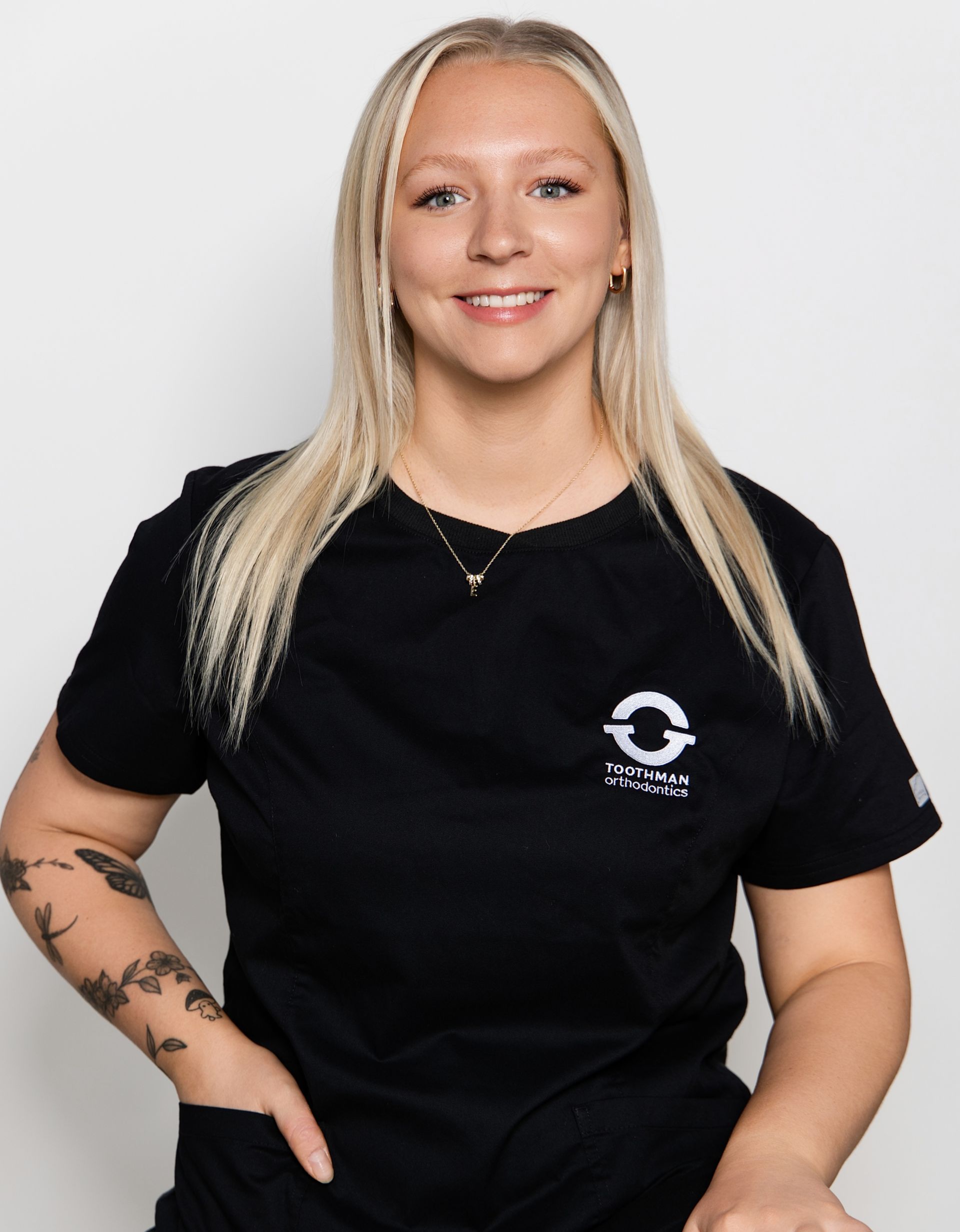 Smiling person in a black t-shirt with tattoos, standing against a light gray background