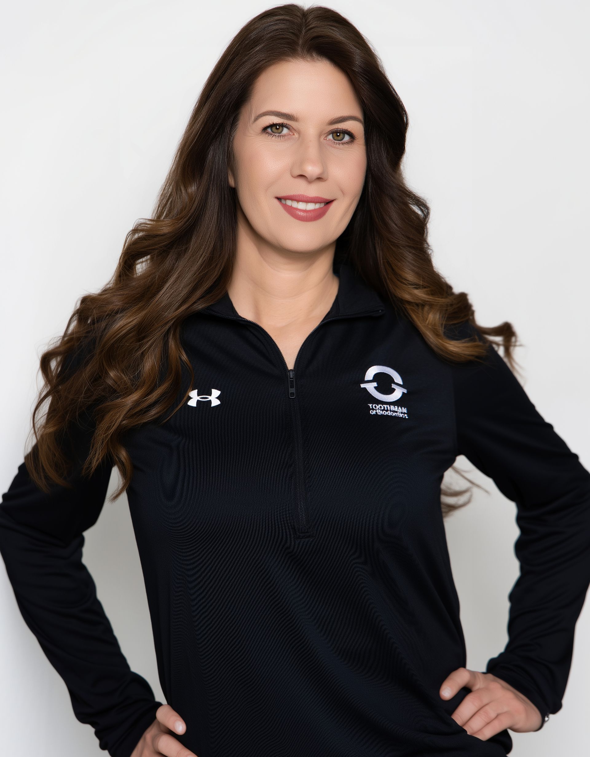 Woman with long brown hair wearing a black zip-up athletic jacket and smiling against a white background