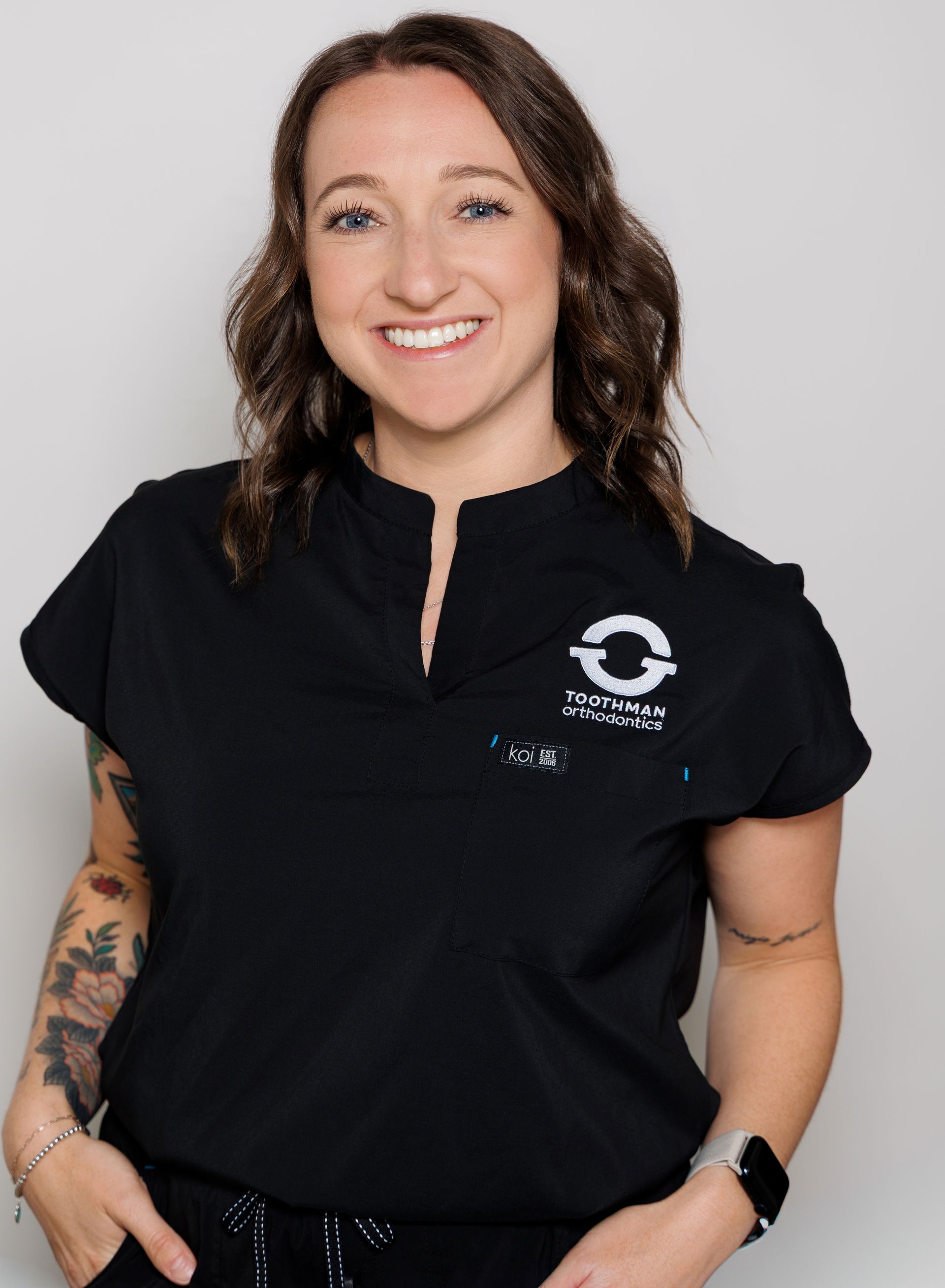 Smiling person in a black polo shirt with a logo, standing against a light gray background