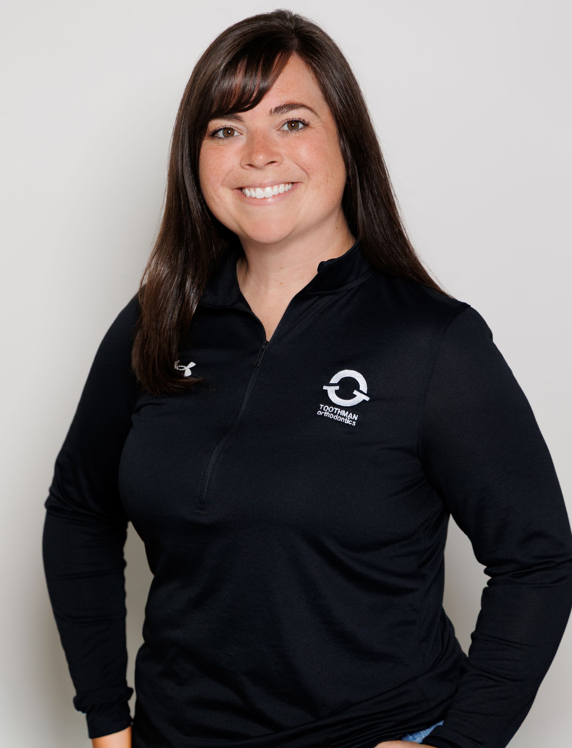 Smiling person in a black collared shirt with a logo, standing against a light background.