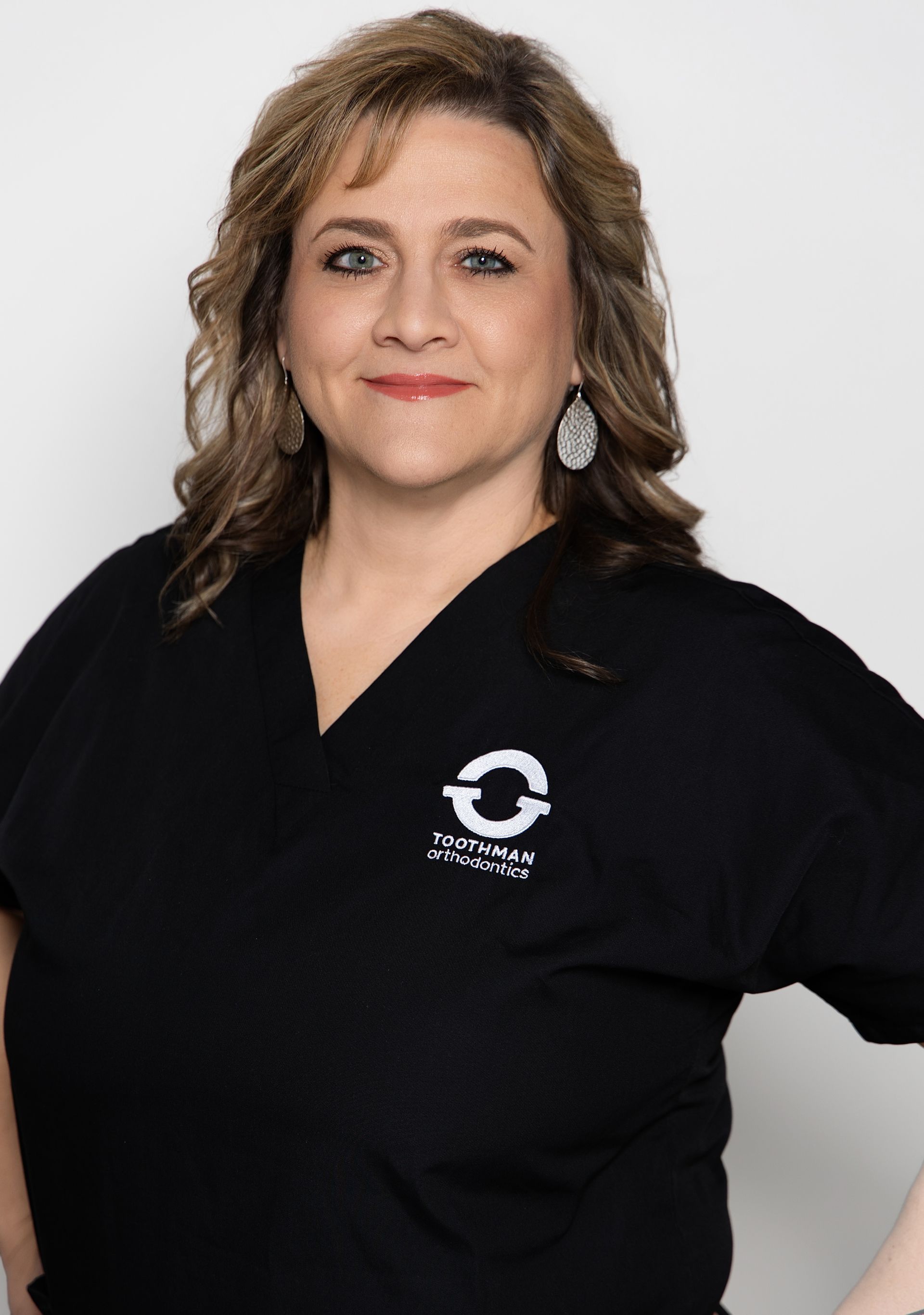 Woman in a black polo shirt with a company logo, standing against a plain light background.