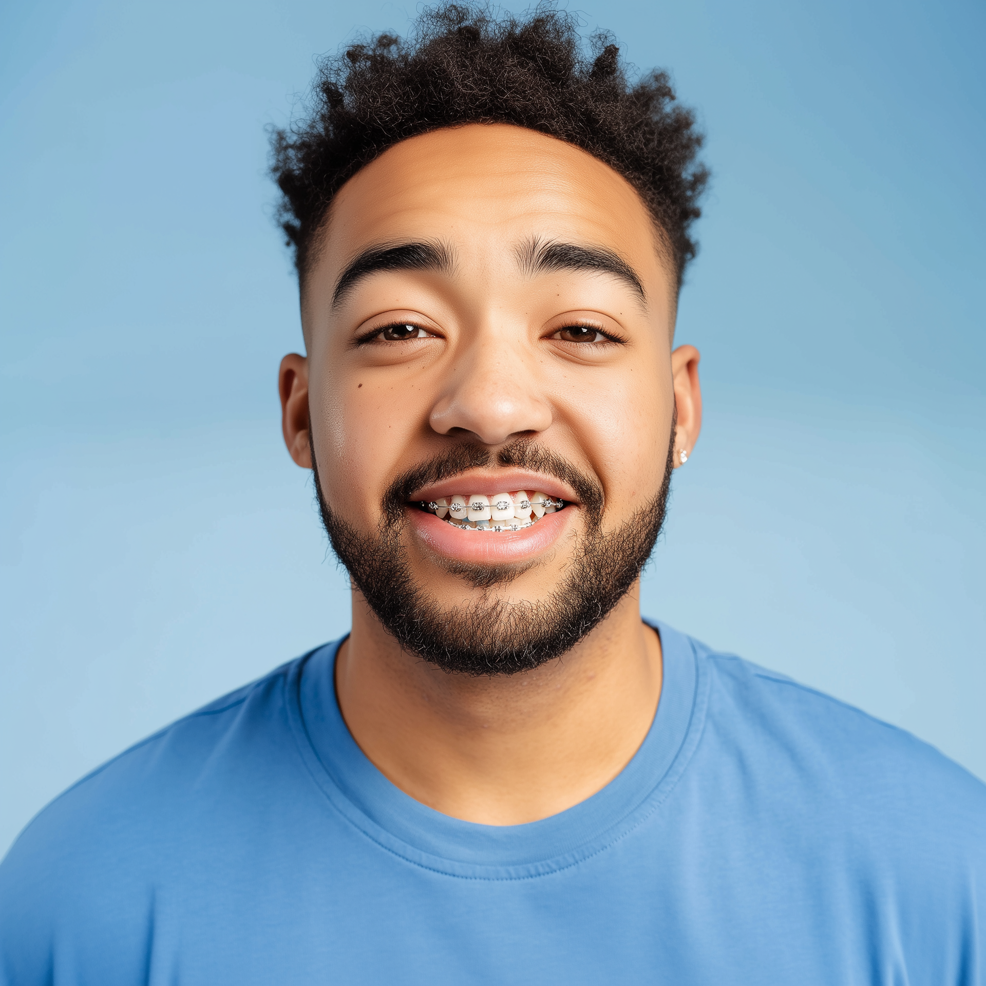 Smiling man in a blue shirt against a light blue background, showing braces