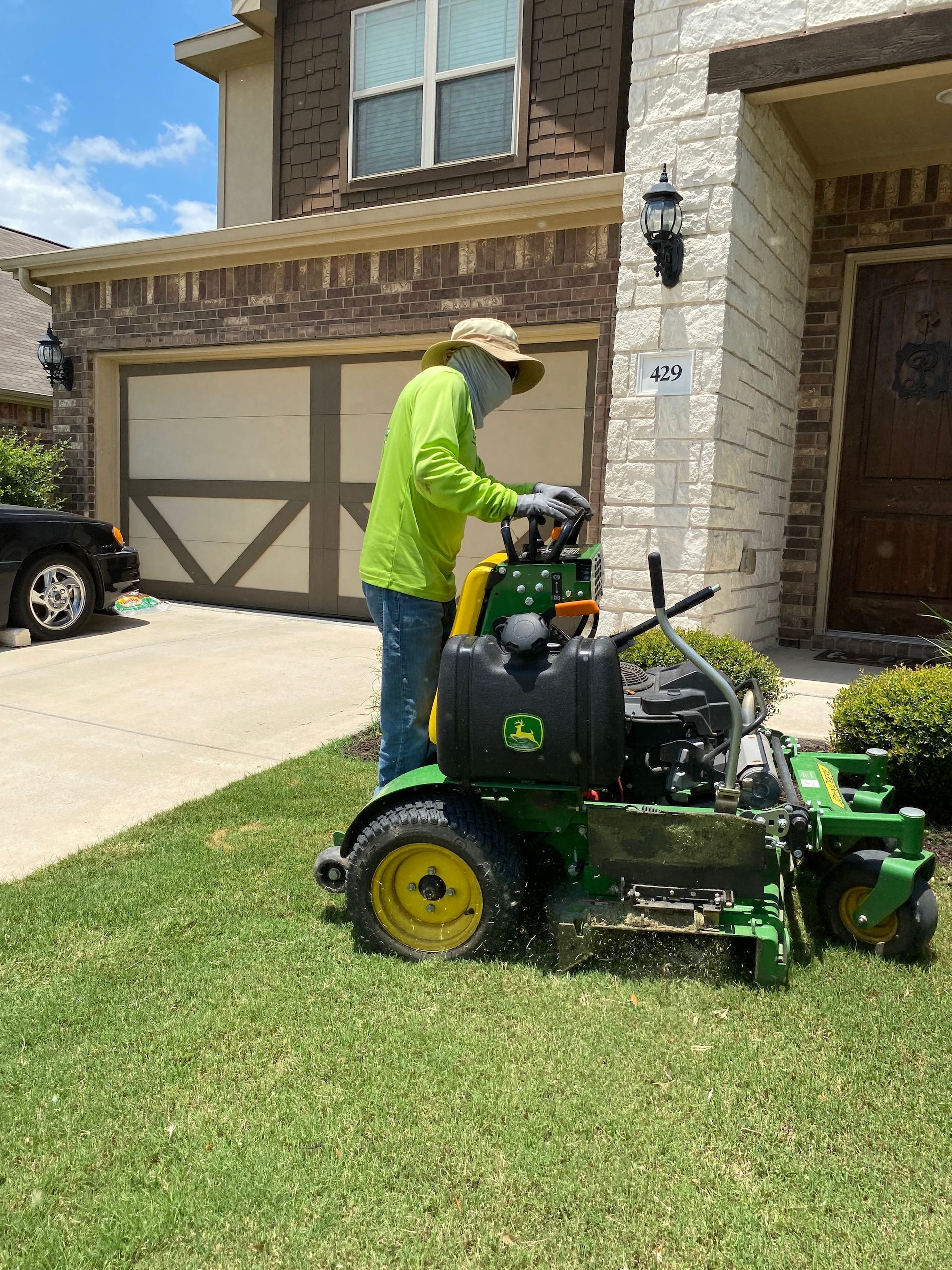 a man is using a john deere lawn mower to cut the grass in front of a house .