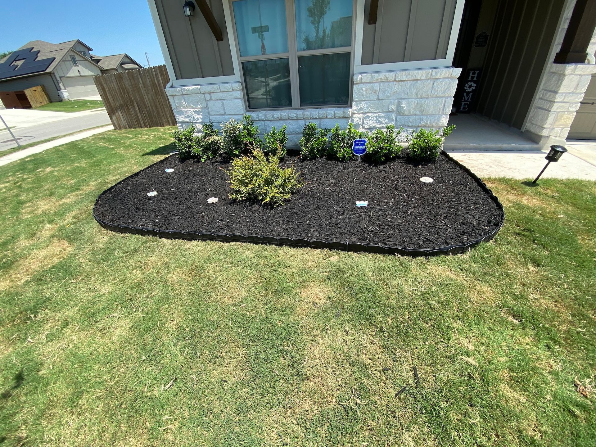 a lawn with a bed of mulch and plants in front of a house .