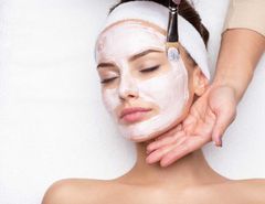 Woman with a facial mask applied by a hand holding a brush.