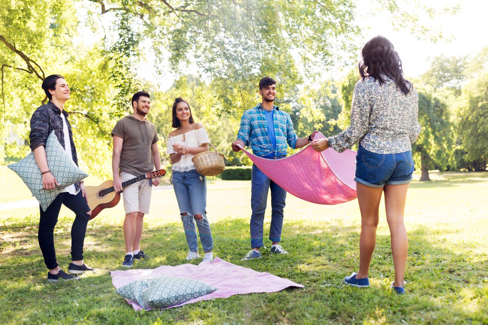 Friends in a park setting, preparing a pink picnic blanket, sunny day.