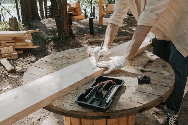 Person in white gloves assembling a wooden board on a round table outdoors with tools nearby