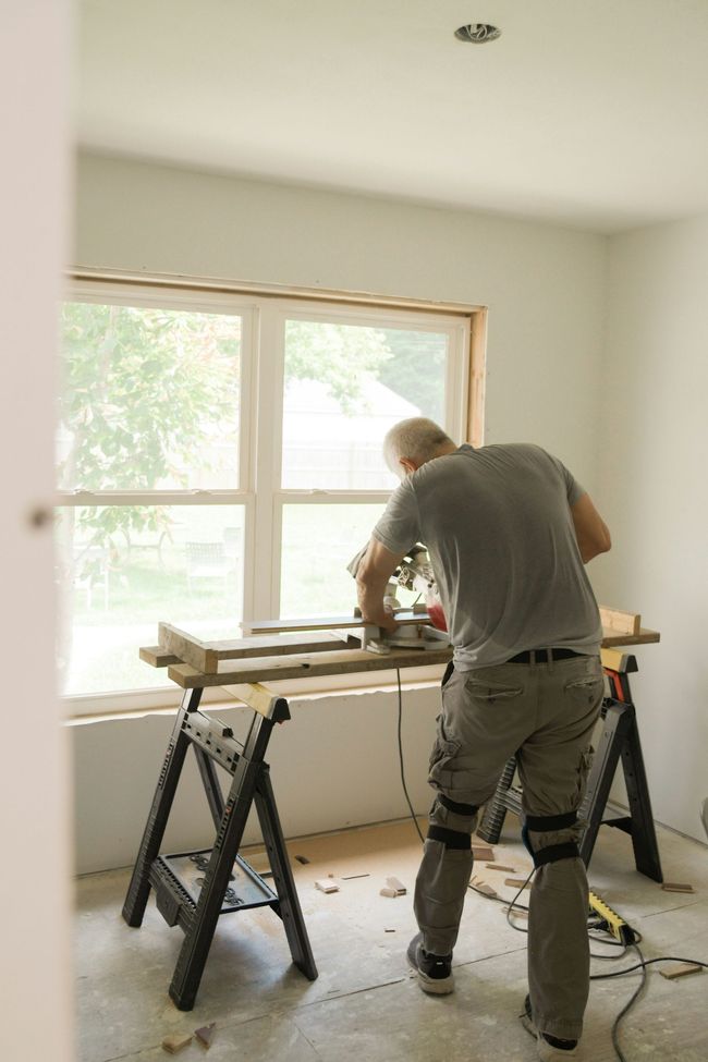 Person working on a wooden table in a bright room with a large window