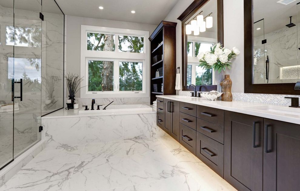 Bright modern bathroom with marble floors, dark wood vanity, large mirror, and frosted glass shower.