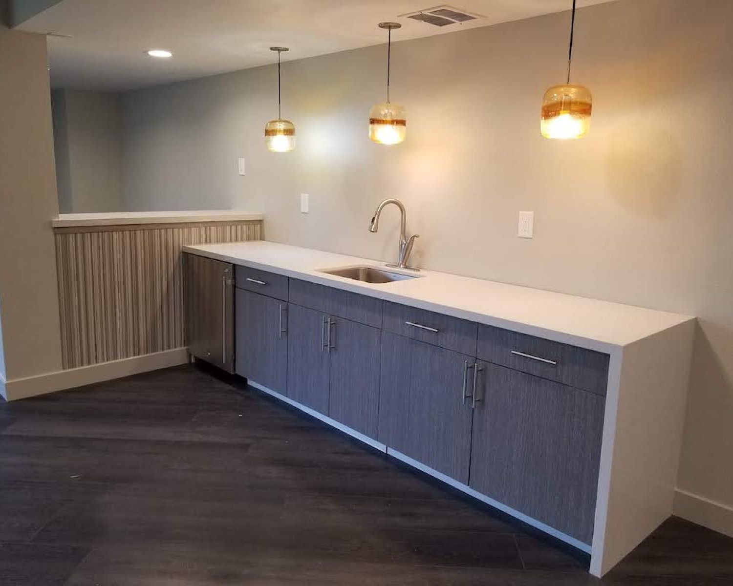Modern kitchen with white countertop, gray cabinets, pendant lights, and dark wood flooring.