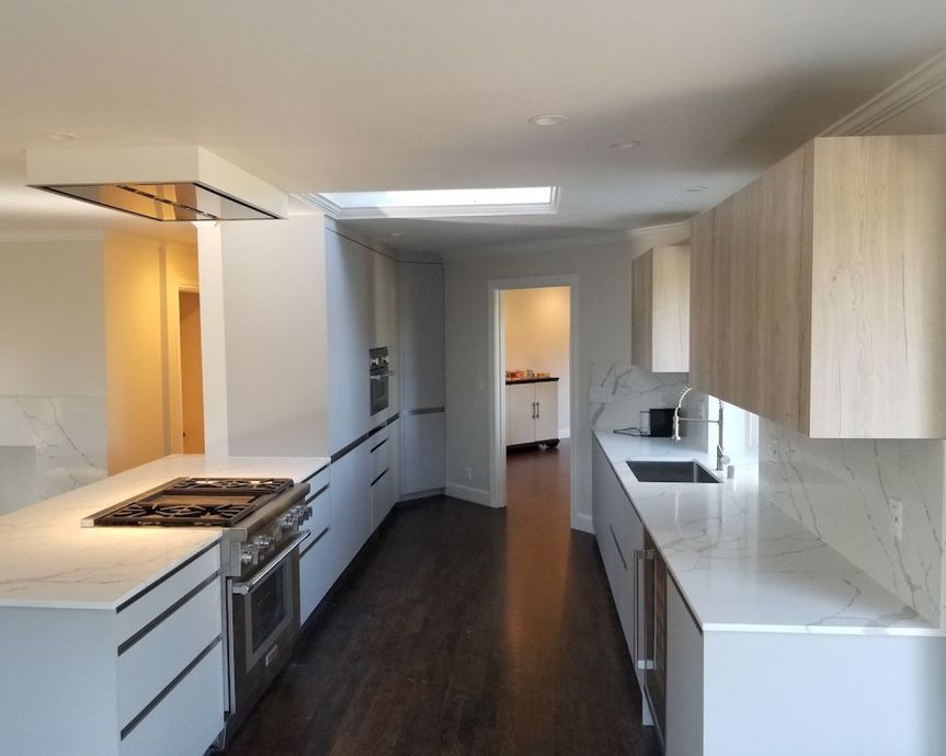 Modern white galley kitchen with island, stainless stove, wood floors, and light wood cabinets