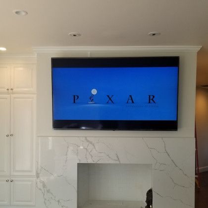 Wall-mounted TV in a white living room shows the Pixar logo above a marble fireplace.