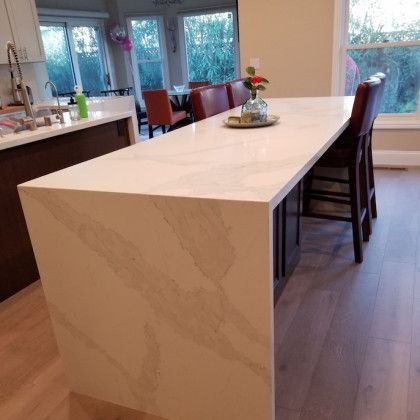 Modern kitchen with a long white island, bar stools, and a dining area by large windows