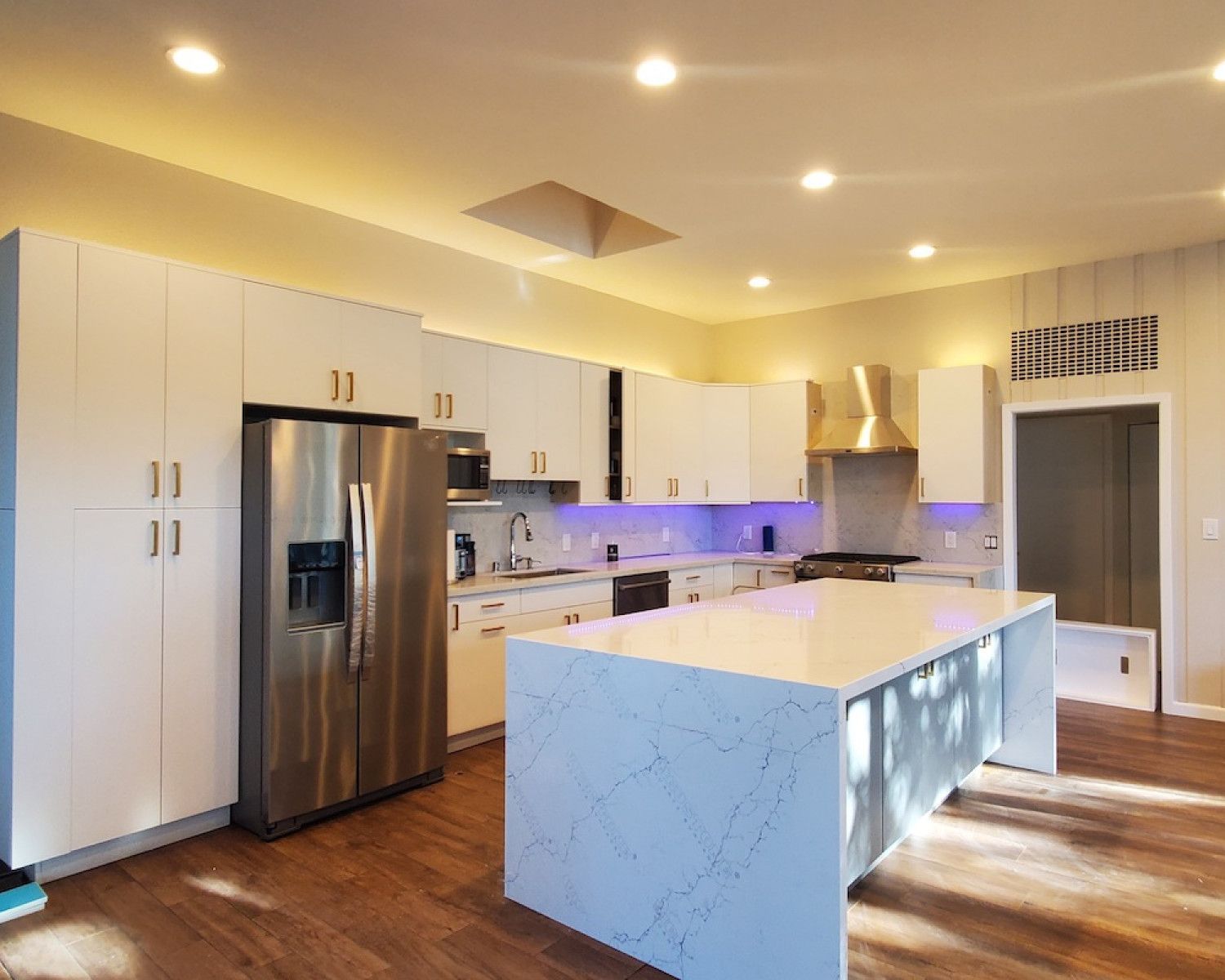 Modern white kitchen with stainless steel appliances, marble island, recessed lighting, and wood floors