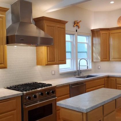 Modern kitchen with wood cabinets, stainless steel stove and hood, window over sink, and gray island countertop