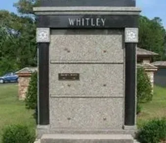 White stone monument sign reading “WHITLEY” in a grassy outdoor setting.