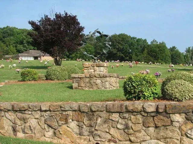 Stone garden wall and flower beds in a green park under a cloudy sky