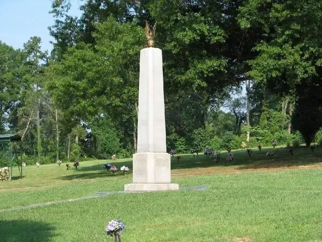 Stone monument in a grassy park with trees in the background and a small flower arrangement in front