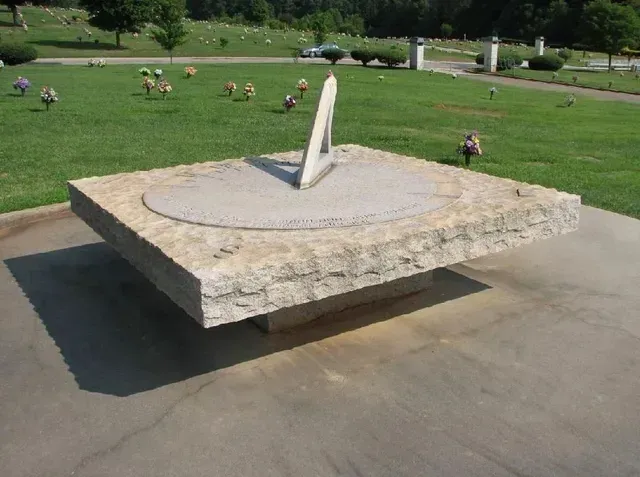 Large stone sundial sculpture on a concrete pad in a grassy park