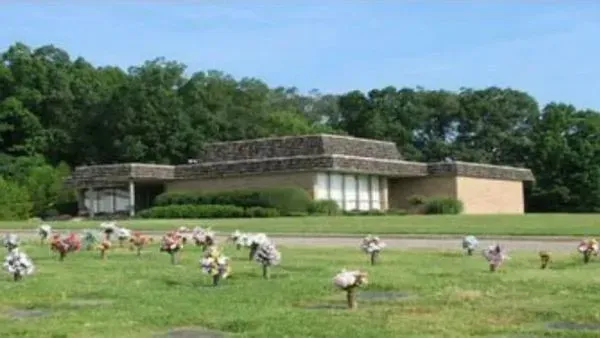 Low modern building beside a grassy field with flower sculptures and trees in the background