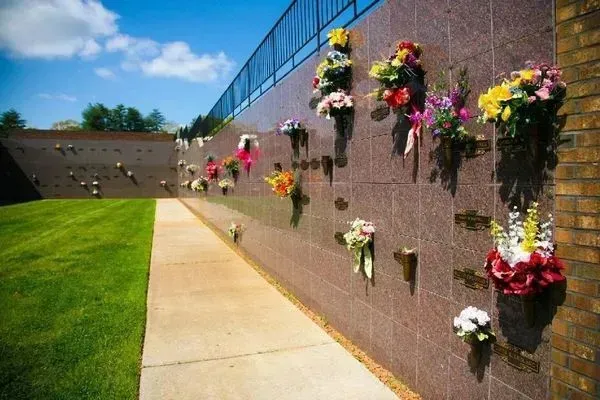Memorial wall with colorful flower bouquets beside a sunny sidewalk and green lawn