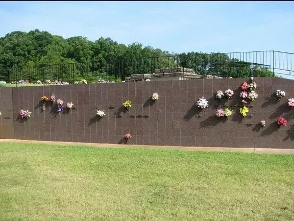 Flower-covered brick wall beside a green lawn and trees under a clear sky