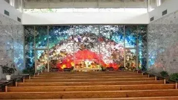 Wooden church pews facing a colorful abstract mural behind the altar.