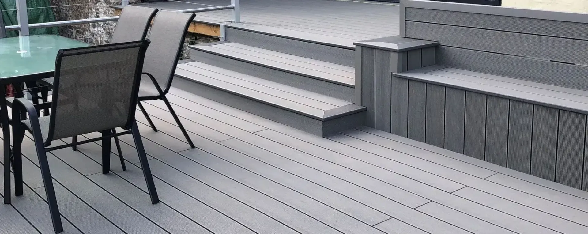 A gray deck with a built-in bench, stairs, and patio furniture.