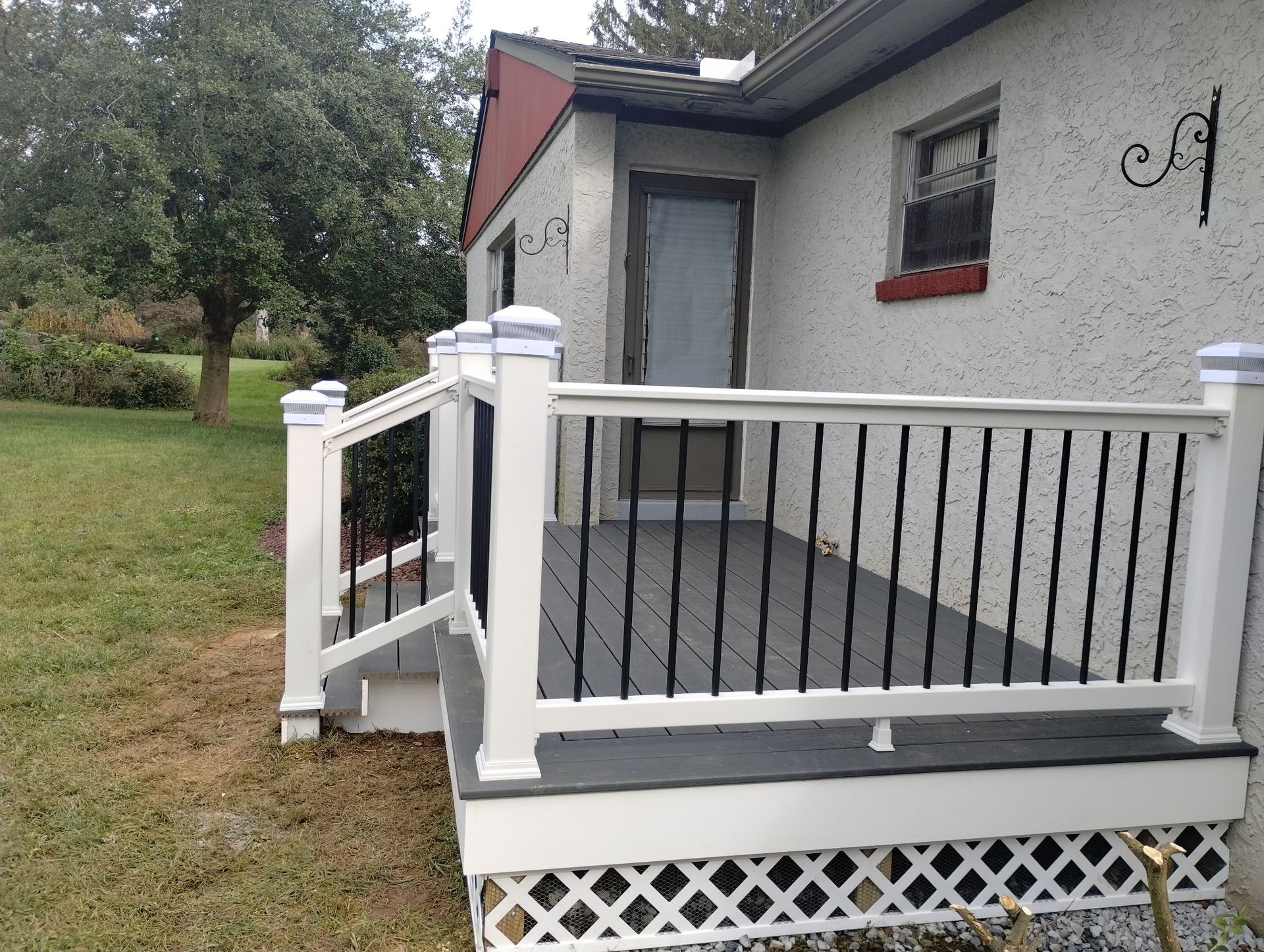A small white deck with black railings and a latticed base next to a stucco house.