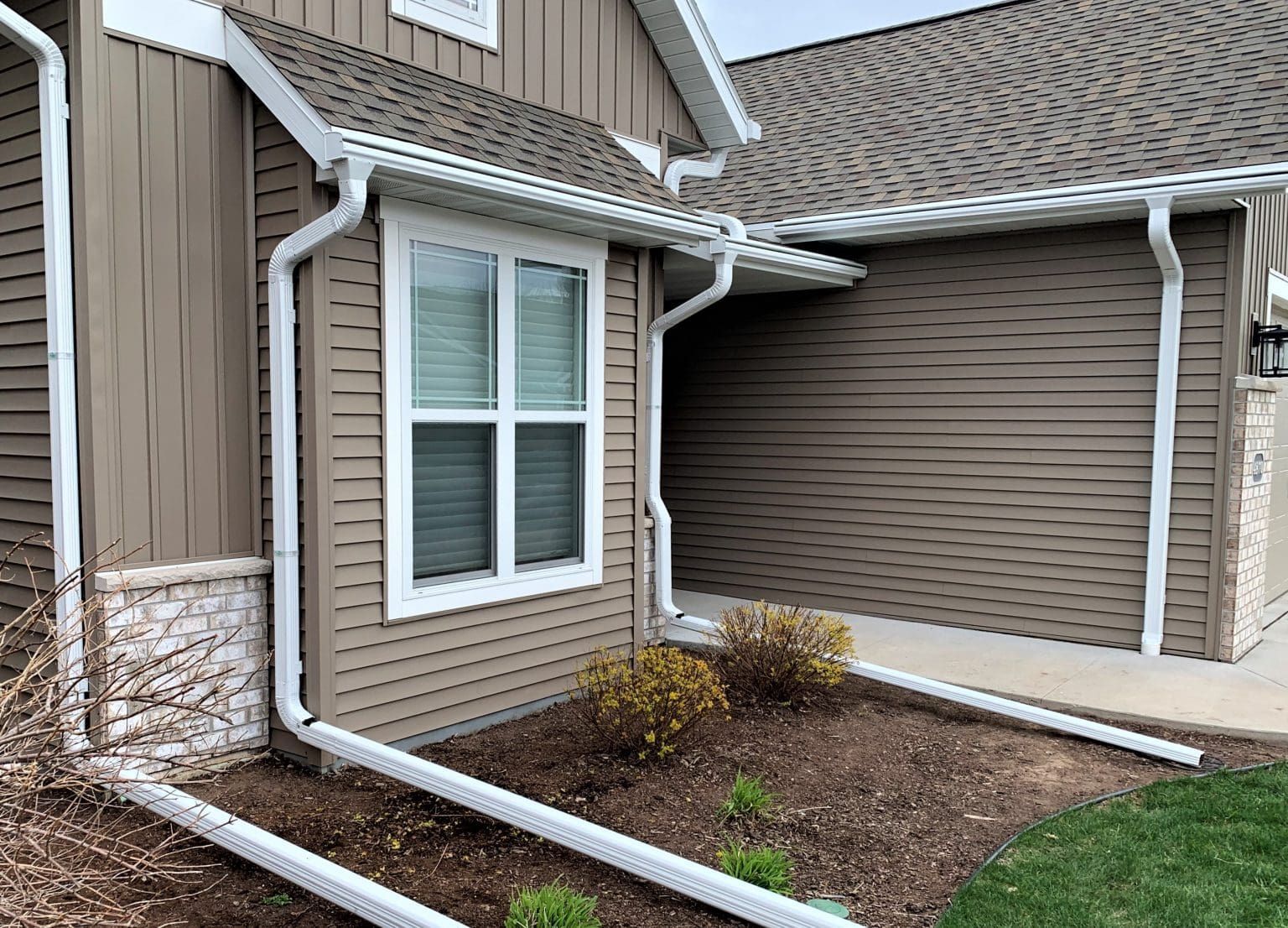 Brown house with white gutters, window, and landscaping.