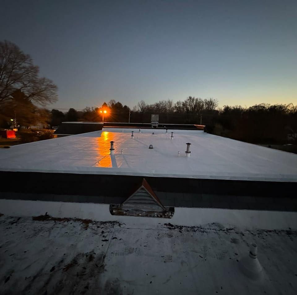 Flat, white commercial roof reflecting warm light at dusk. Several vents and a small structure are visible.
