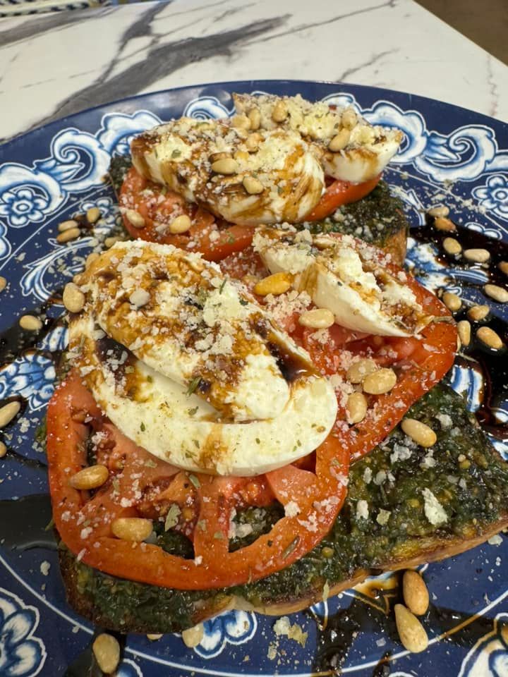 Bruschetta with pesto, tomato, mozzarella, pine nuts, and balsamic glaze, served on a blue patterned plate.