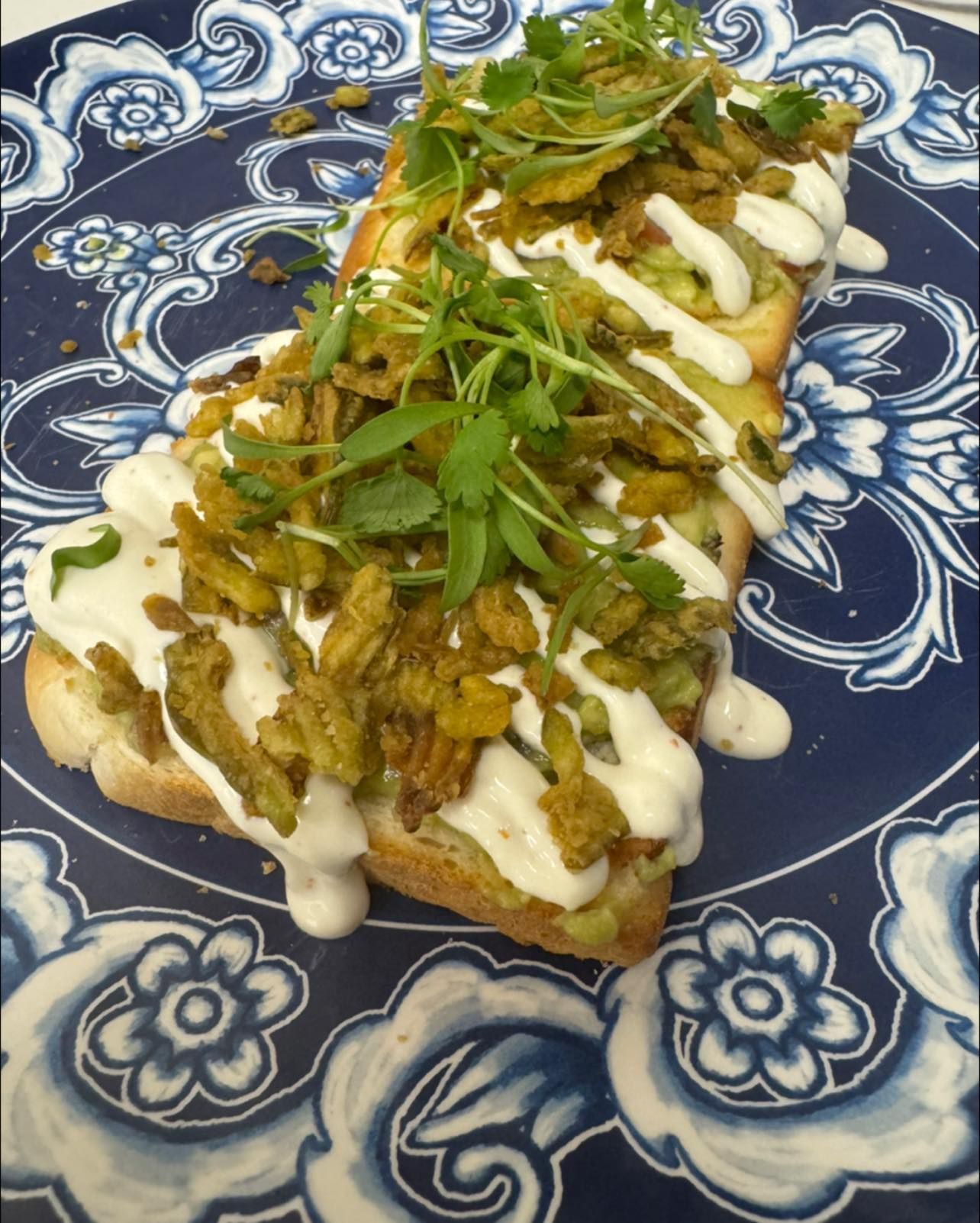 Toast topped with avocado, fried onion, and white sauce on a blue patterned plate.