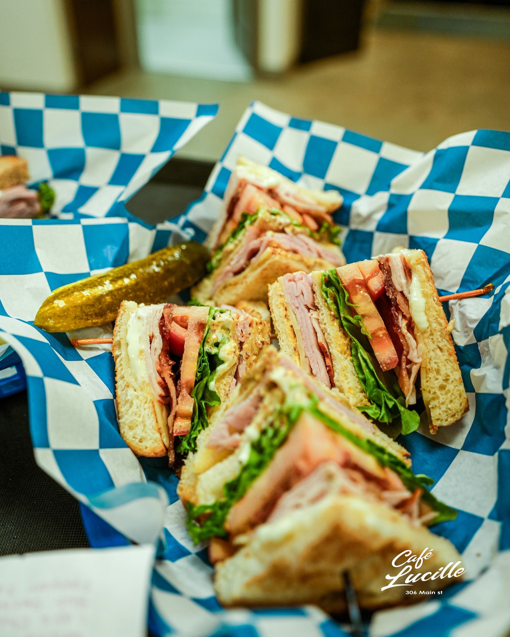 Club sandwiches with pickle in a blue and white checkered basket.