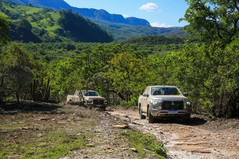 Dois SUVs brancos em uma estrada de terra em um vale montanhoso verdejante.