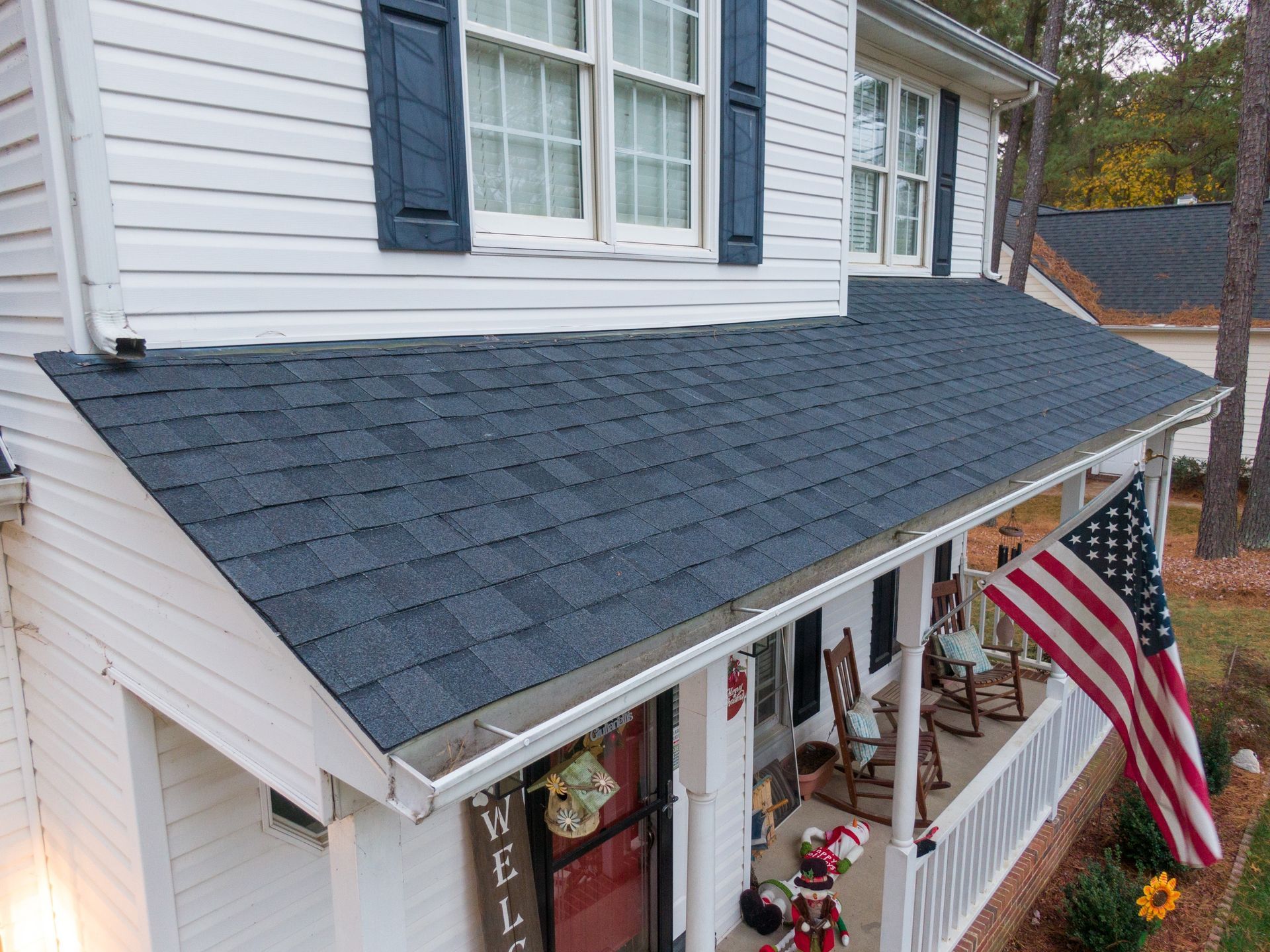 White house with blue shutters, gray roof, front porch, and an American flag hanging outside