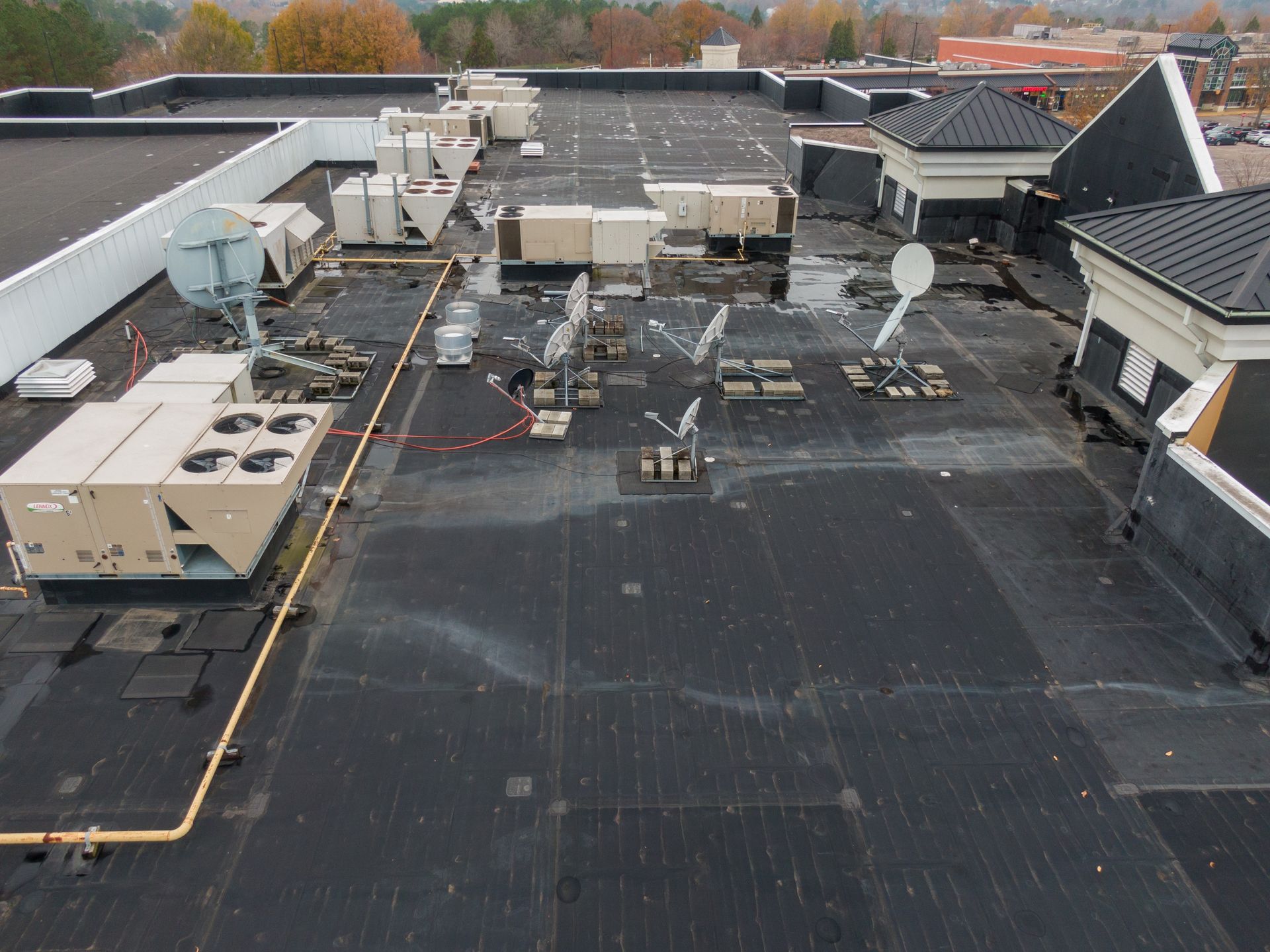 Rooftop with HVAC units, satellite dishes, and pipes on a flat commercial building.