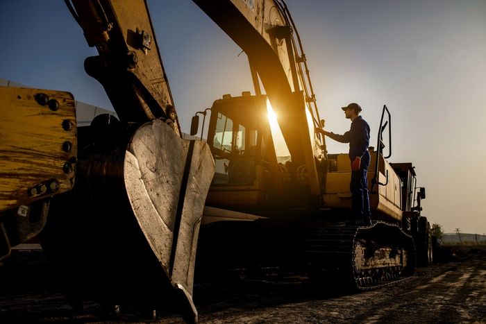 A man is standing next to a large excavator on a construction site.