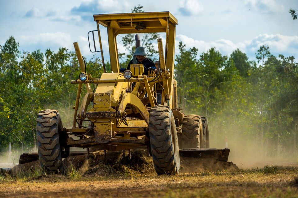A man is driving a yellow tractor through a dirt field.