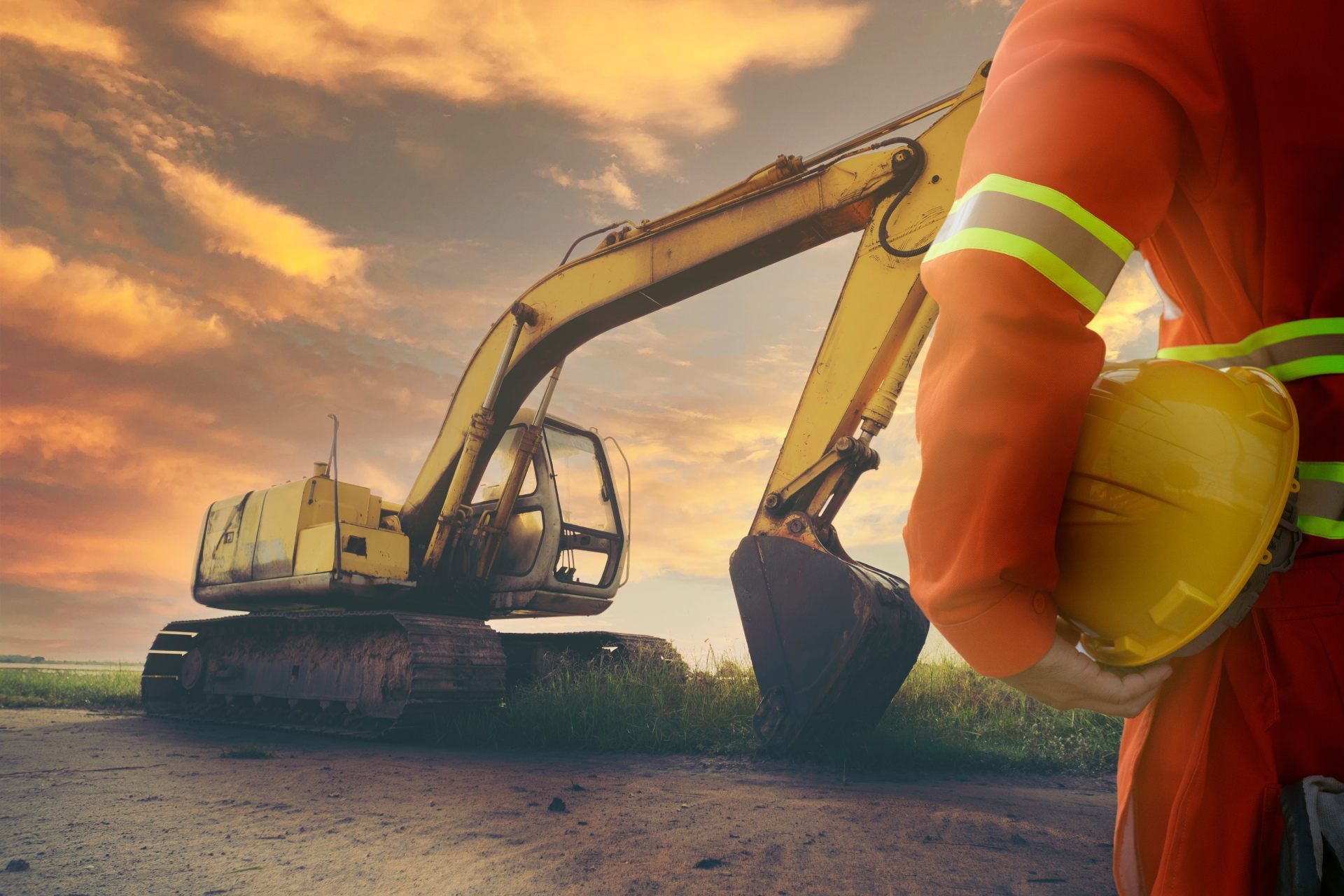 A construction worker is holding a hard hat in front of an excavator.