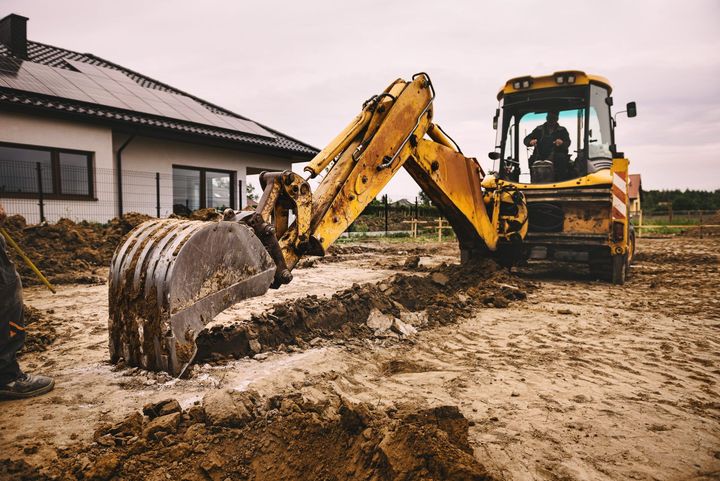 A yellow excavator is sitting on top of a pile of dirt at a construction site.